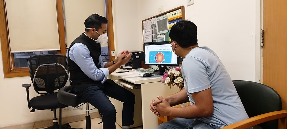 Two men in an office discuss, wearing masks; a computer monitor shows a brain image, suggesting a medical consultation about neurology or brain health.