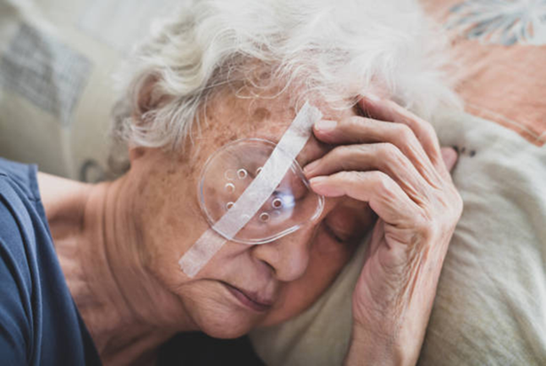 Older woman lying in bed with a clear eye patch taped over her eye.