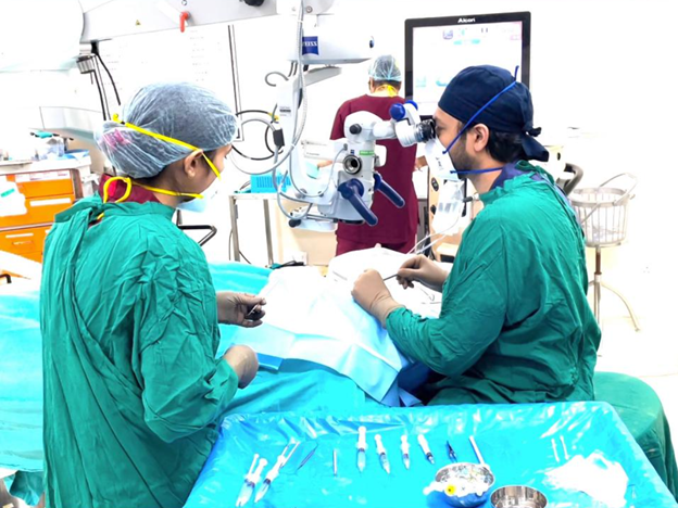 Two surgeons in green scrubs perform surgery at a patient’s operating table with medical equipment surrounding them.